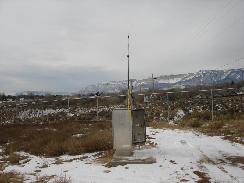 Antenna situated on a small, grey metal power box in a snowy winter landscape with mountains in the background