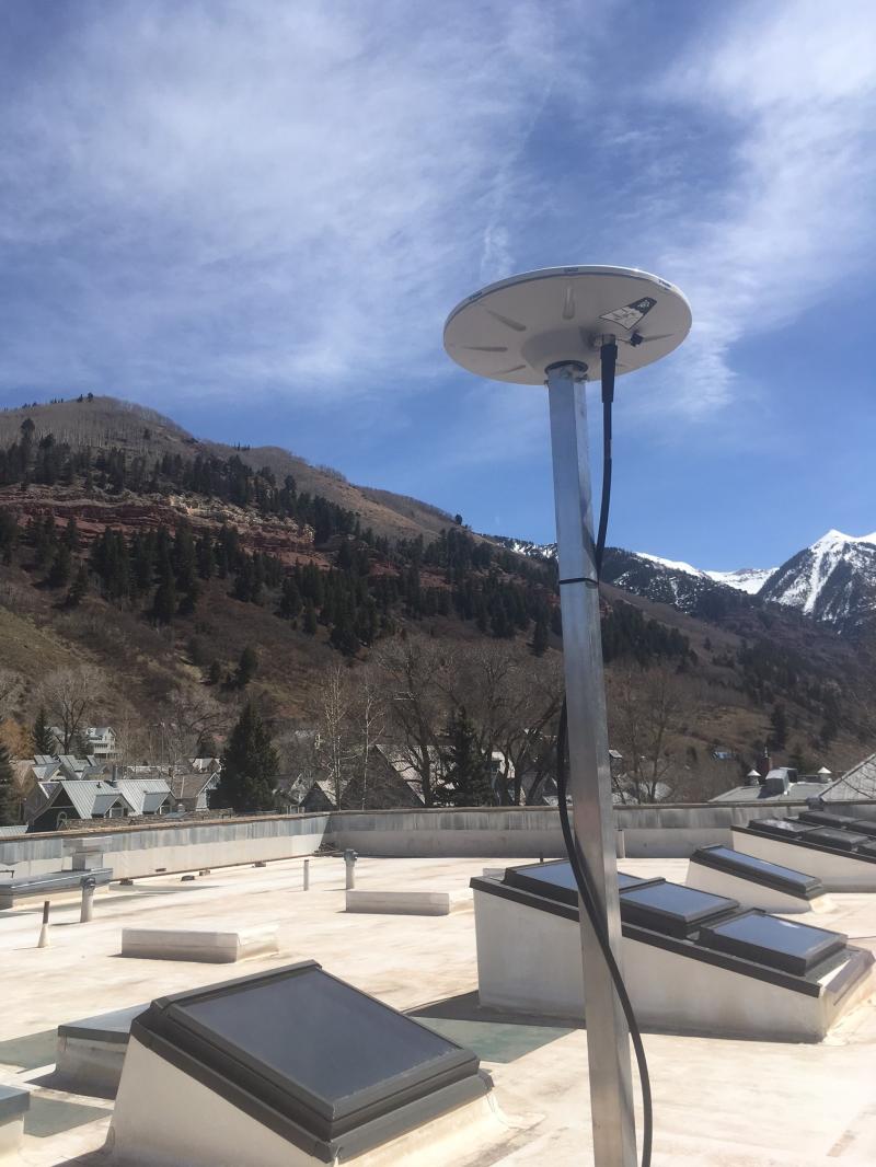 Antenna located on a flat, white roof with mountains and a blue sky in the background.