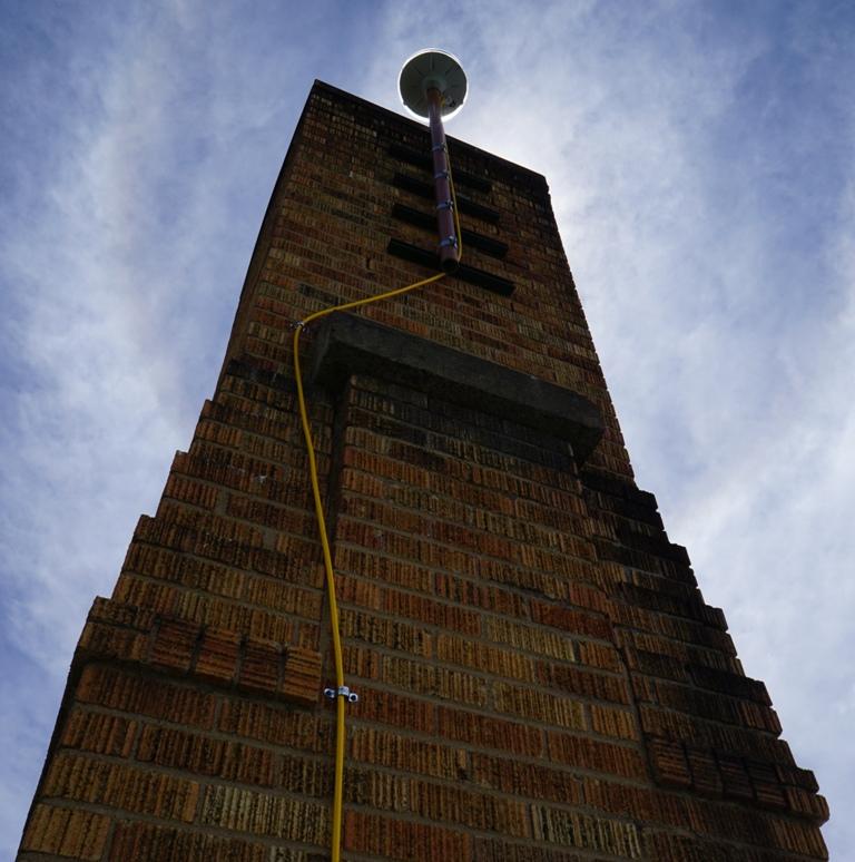 Antenna attached to large brick tower with a background of blue sky and wispy white clouds.