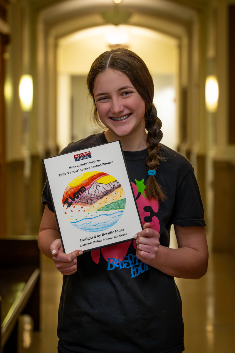 Middle school student holds up plaque with her winning "I Voted" Sticker Design. 