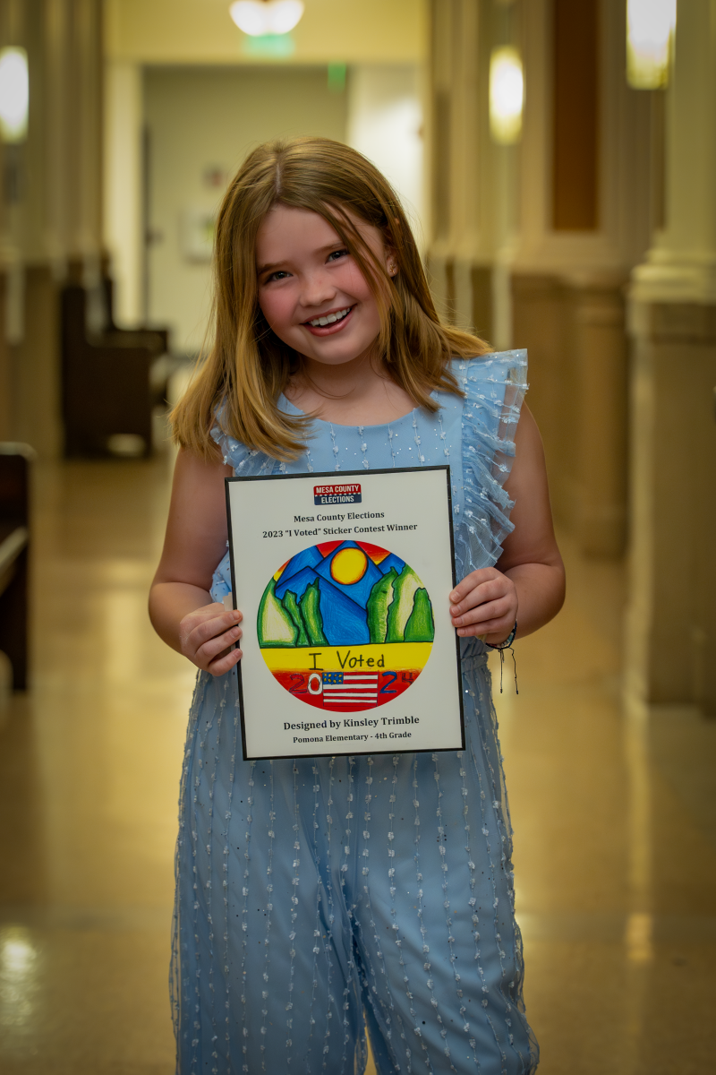 Elementary student holds up plaque with her winning "I Voted" Sticker Design. 