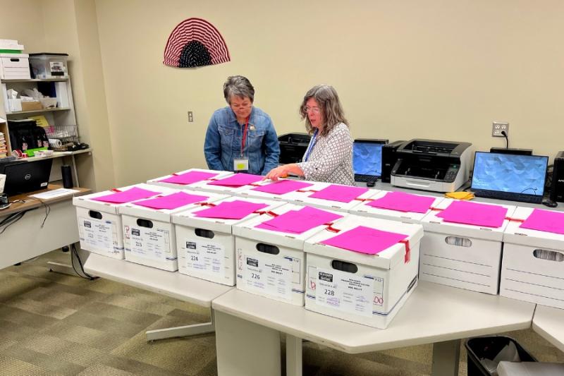 Two people reviewing boxes of ballots. 