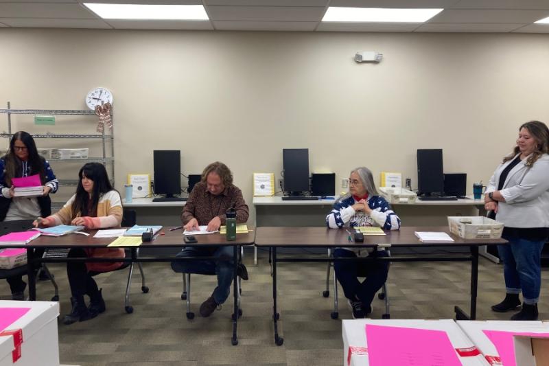 People sit at long table reviewing ballots. 