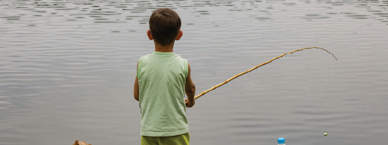 A young boy is facing away from the camera as he fishes in a pond.