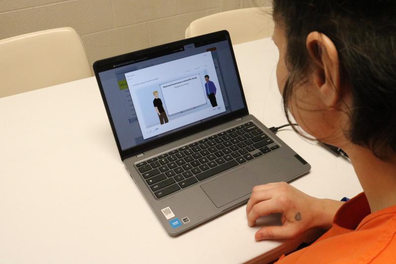 A female inmate sits at a table with a computer studying for the GED.
