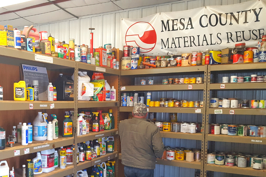 Man looking at products at the Hazardous Waste Collection Facility with sign in the background reading Mesa County Materials Reuse.