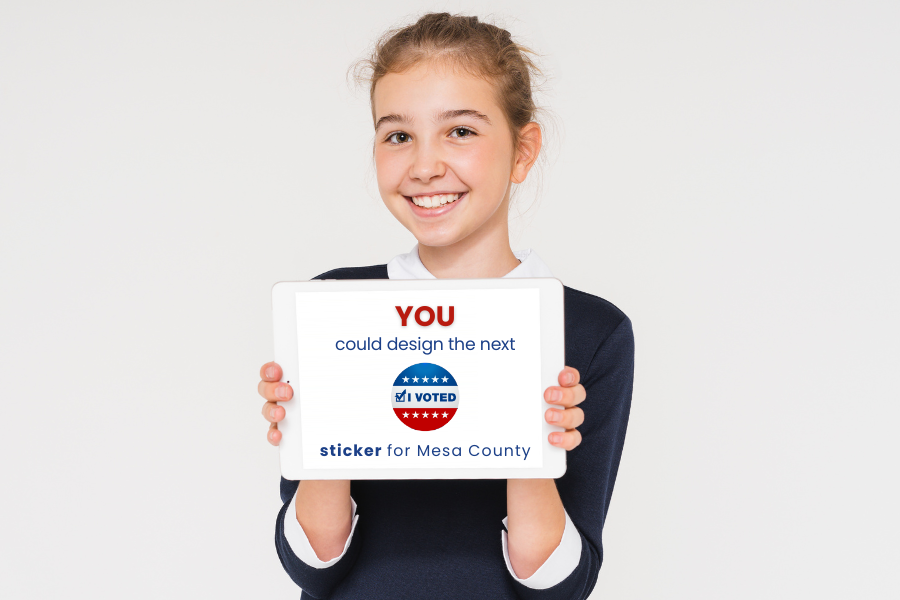 Child holding IPad that reads "YOU could design the next 'I Voted' sticker for Mesa County".