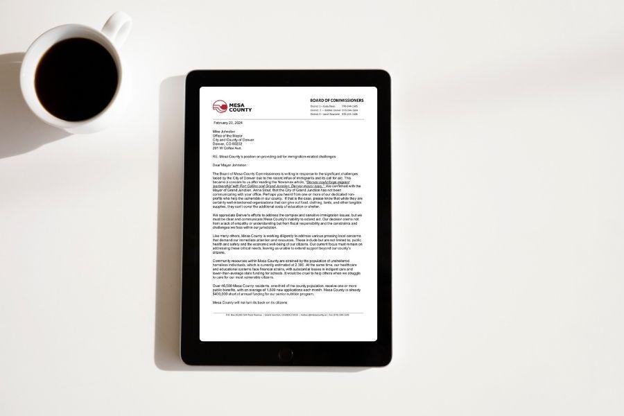 Black IPad displays a Mesa County letter sitting next to a cup of coffee. 